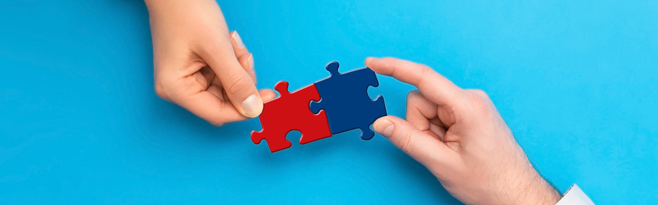 2 Hände stecken ein rotes und ein blaues Puzzleteil zusammen.