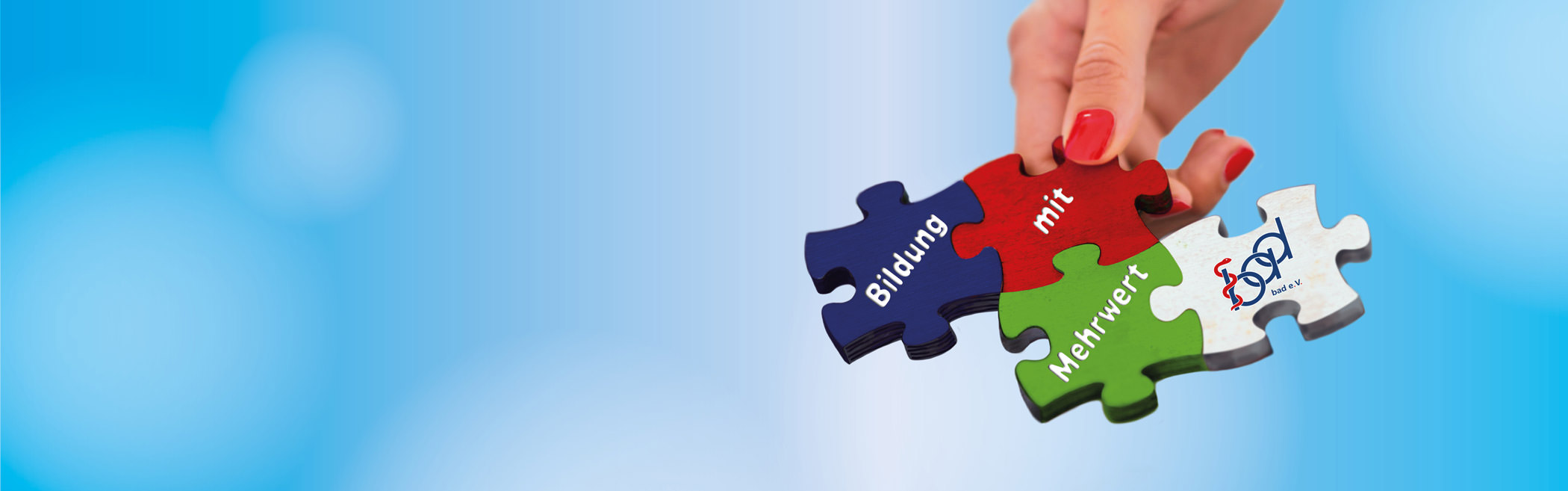 Bild eines Puzzles, das von einer Hand gehalten wird, mit einem blauen Himmel im Hintergrund. Die Puzzleteile sind rot, weiß, grün und blau und tragen die Aufschriften 'Bildung mit Mehrwert' sowie das Logo des bad e. V., das eine Verbindung zwischen den Elementen symbolisiert.